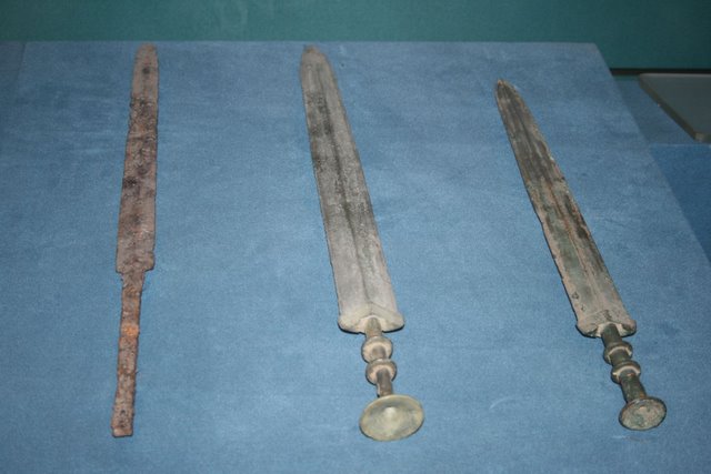 An iron sword and two bronze swords of the Chinese Warring States period, laid side by side against a plain ground